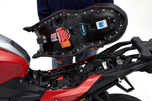 a person holding Canyon Dual Sport seat showing the back side heater wiring, MPN printed and mounting brackets pre-installed