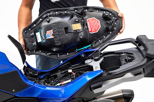 a person holding Canyon Dual Sport seat showing the back side heater wiring, MPN printed and mounting brackets pre-installed