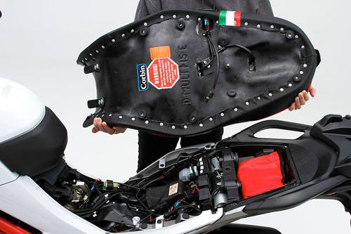 a person holding Canyon Dual Sport seat showing the back side heater wiring, MPN printed and mounting brackets pre-installed