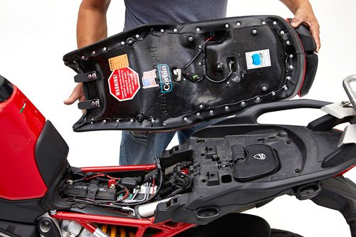 a person holding Canyon Dual Sport seat showing the back side heater wiring, MPN printed and mounting brackets pre-installed