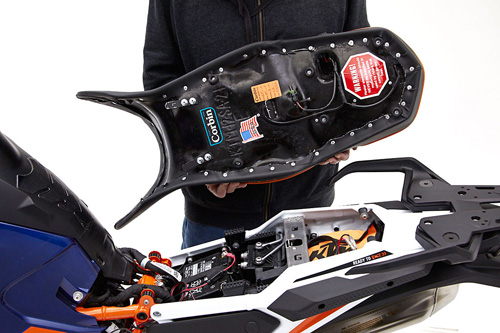 a person holding Canyon Dual Sport seat showing the back side heater wiring, MPN printed and mounting brackets pre-installed