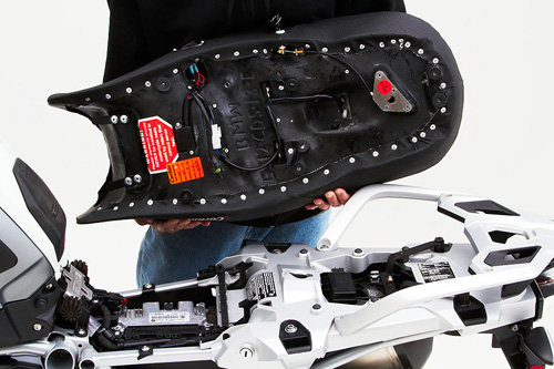 a person holding Canyon Dual Sport seat showing the back side heater wiring, MPN printed and mounting brackets pre-installed