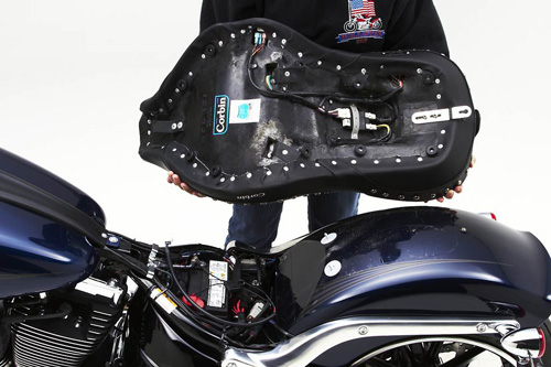 a person holding Dual Touring seat showing the back side heater wiring, MPN printed and mounting brackets pre-installed