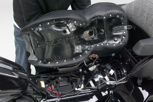 a person holding Dual Touring seat showing the back side heater wiring, MPN printed and mounting brackets pre-installed