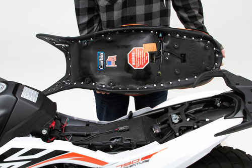 a person holding Canyon Dual Sport seat showing the back side heater wiring, MPN printed and mounting brackets pre-installed