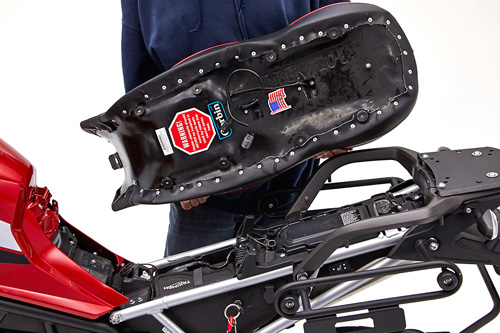 a person holding Canyon Dual Sport seat showing the back side heater wiring, MPN printed and mounting brackets pre-installed