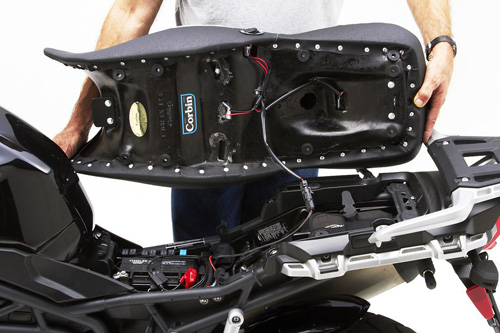 a person holding Canyon Dual Sport seat showing the back side heater wiring, MPN printed and mounting brackets pre-installed