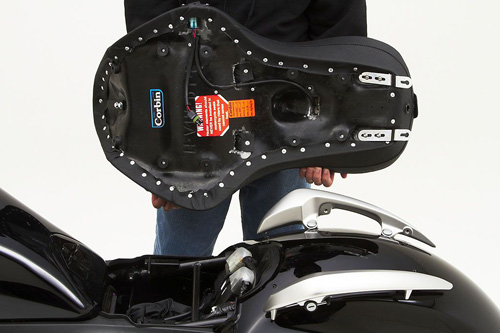 a person holding Dual Tour seat showing the back side heater wiring, MPN printed and mounting brackets pre-installed