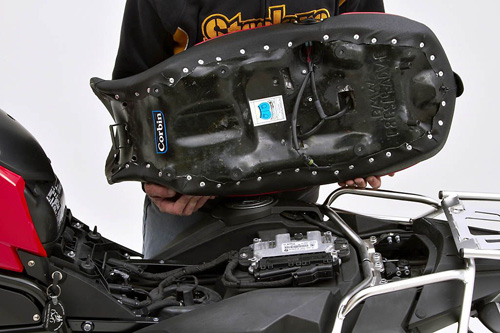 a person holding Canyon Dual Sport seat showing the back side heater wiring, MPN printed and mounting brackets pre-installed