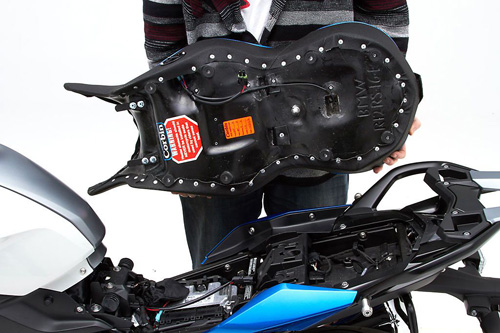 a person holding Canyon Dual Sport seat showing the back side heater wiring, MPN printed and mounting brackets pre-installed