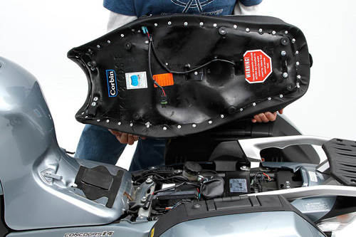 a person holding Canyon Dual Sport seat showing the heater wiring, MPN printed and mounting brackets pre-installed