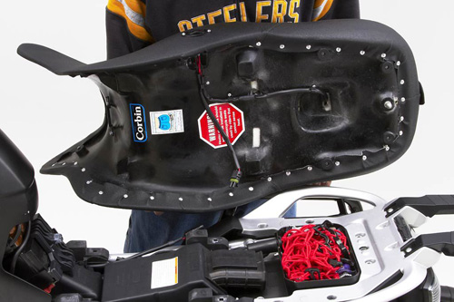 a person holding Canyon Dual Sport seat showing the rear side, MPN printed, heater wiring harness and mounting brackets pre-installed