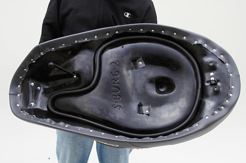 a person holding Dual seat showing the rear side, MPN printed and mounting brackets pre-installed, Latch loop and OEM hinge and key lock is also shown