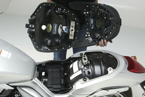 a person holding Front & Rear seat showing the rear side with Corbin sticker, heater wiring harness and mounting brackets pre-installed