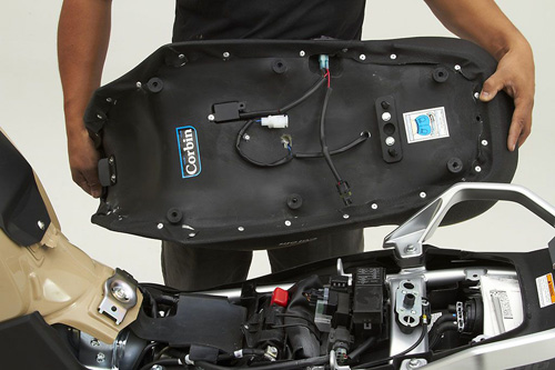 a person holding Canyon Dual Sport seat showing the rear side, Corbin sticker printed, heater wiring harness and mounting brackets pre-installed