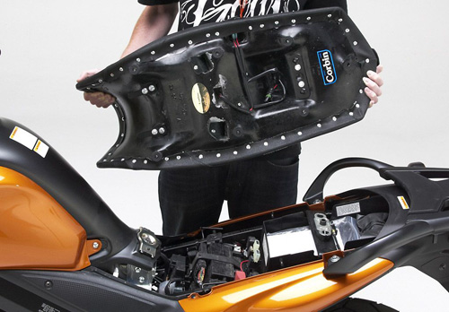 a person holding Canyon Dual Sport seat showing the rear side, MPN printed, heater wiring harness and mounting brackets pre-installed