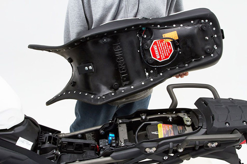 a person holding Canyon Dual Sport seat showing the back side heater wiring, MPN printed and mounting brackets pre-installed