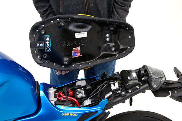 a person holding Gunfighter & Lady seat showing the rear side with MPN/Corbin sticker printed and mounting brackets pre-installed