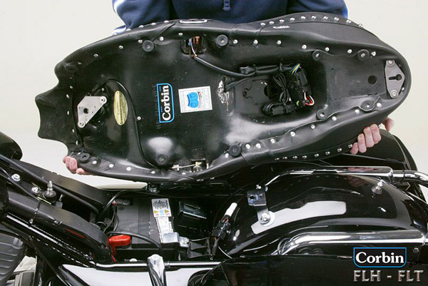 a person holding Dual Touring seat showing rear side with MPN printed, heater wiring, keylock system and mounting brackets pre-installed