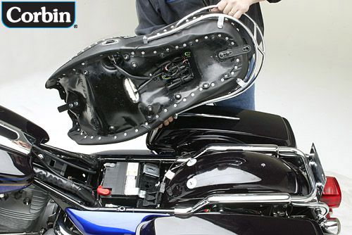 a person is holding Dual Tour seat showing rear side MPN printed, heater wiring harness and mounting brackets pre-installed