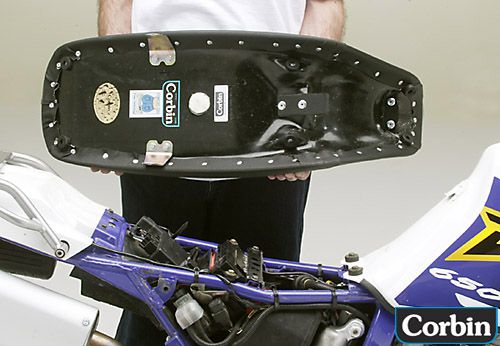 a person is holding  Dual sport seat showing basepan with mounting brackets pre-installed