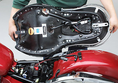 a person is holding Dual Tour seat showing rear side MPN printed, heater wiring and mounting brackets pre-installed