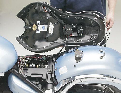 a person is holding Dual Tour seat showing basepan with MPN printed, heater wiring and mounting brackets pre-installed