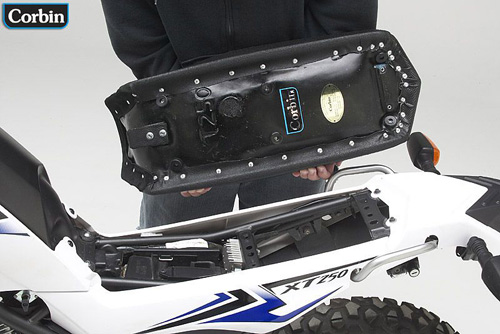 a person is holding Dual Tour seat showing basepan with MPN printed and mounting brackets pre-installed