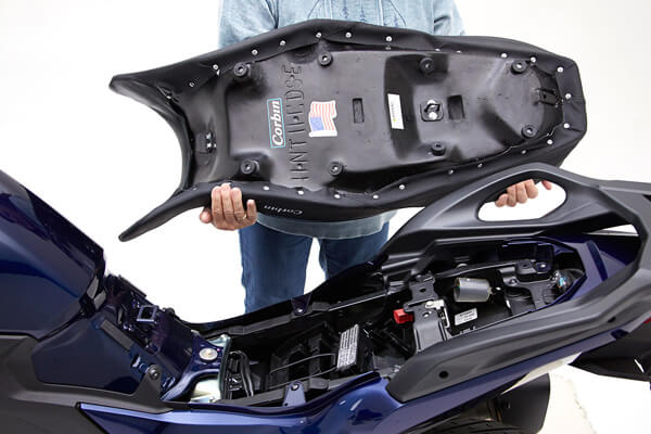 a person is holding dual sport seat showing rear side MPN printed, wiring harness and mounting brackets pre-installed