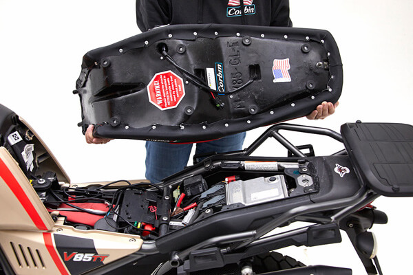 a person is holding Dual Sport Seat showing rear side MPN printed, wiring harness and mounting brackets preinstalled