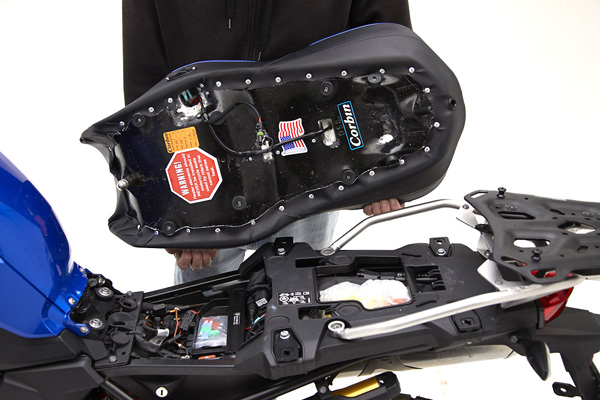 a person is holding seat showing rear side MPN printed, wiring harness and mounting brackets pre-installed
